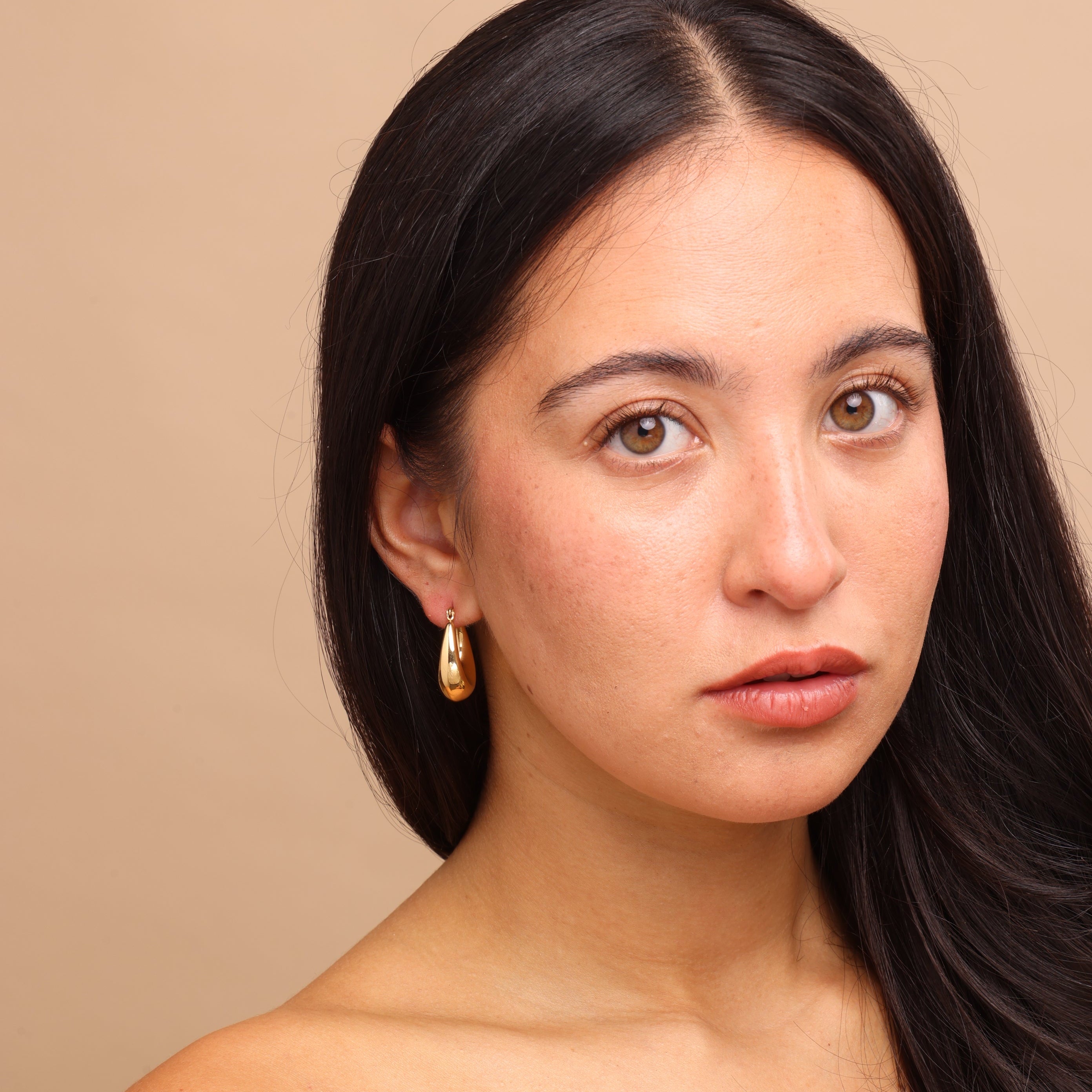 Front view of model in Zoi Era Gold Thick Oval Hoop Earrings β bold oval gold hoops, anti-tarnish waterproof jewellery, essential fashion accessory.