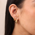 Close-up of a person wearing gold hoop earrings with a neutral background