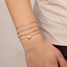 Close-up of a wrist wearing multiple gold bracelets on a neutral background
